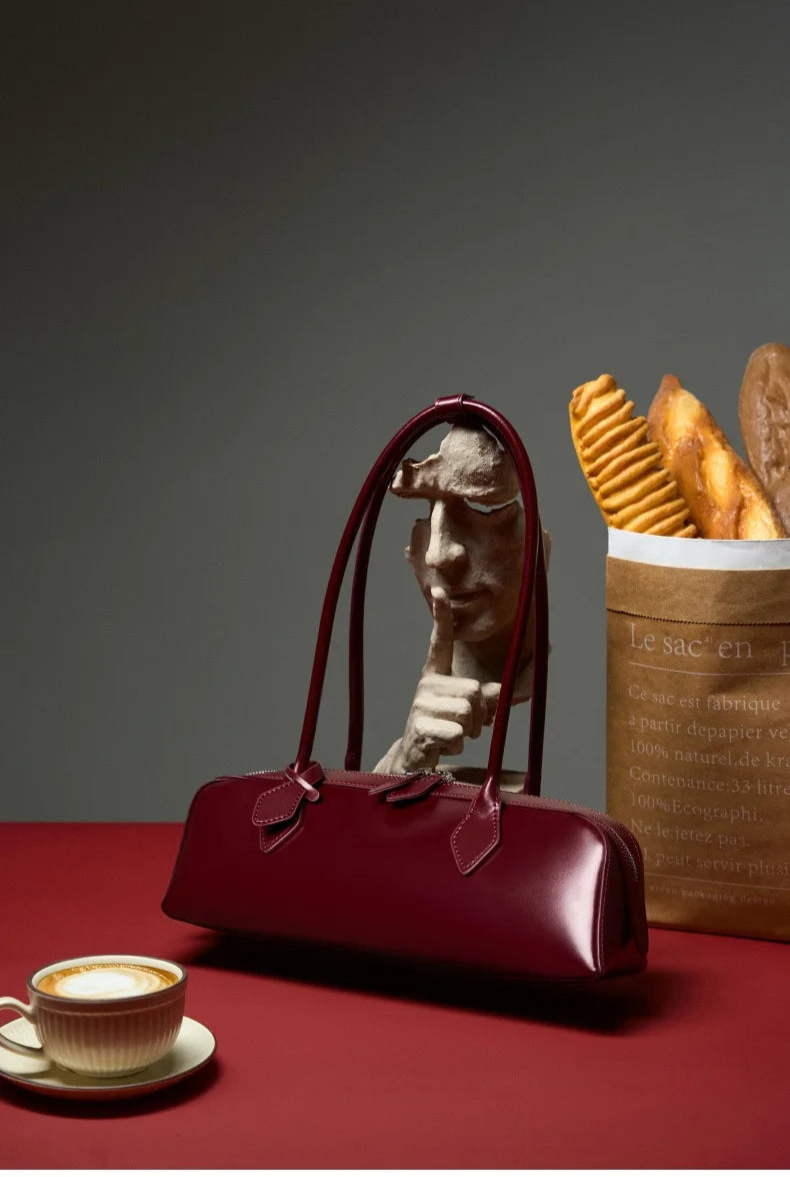 Stylish ladies baguette shoulder bag in burgundy color on a table with coffee and pastries