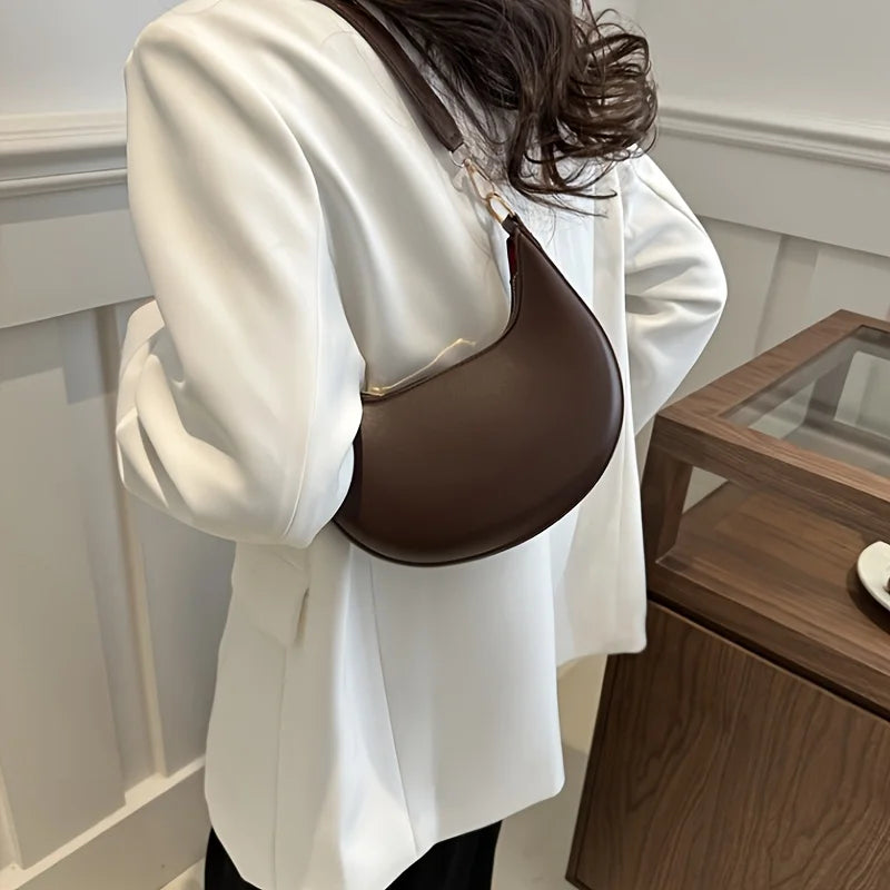 Brown luxury moon-shaped handbag worn on shoulder with elegant outfit for stylish occasions