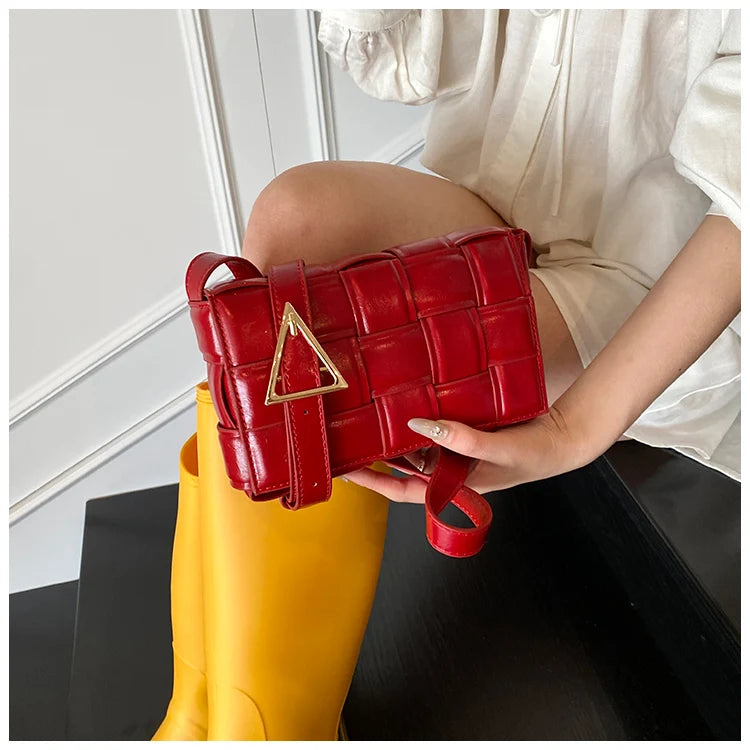 VaultHaus red women's designer shoulder bag with gold triangle buckle held by person wearing white outfit and yellow boots