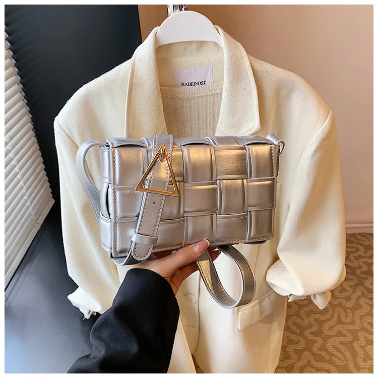 VaultHaus women's designer shoulder bag in metallic silver with woven pattern and gold buckle held over cream jacket