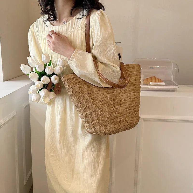 A stylish woman holding a bouquet while carrying a luxury woven shopper tote in a light setting