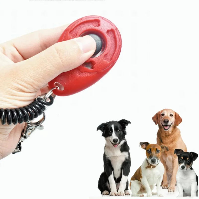 Hand pressing a red dog training clicker with three attentive dogs in the background