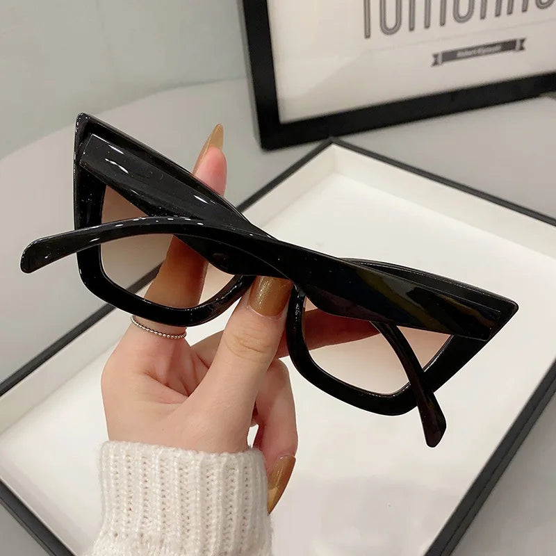 VaultHaus black vintage cat eye sunglasses for women held in hand with beige sweater background