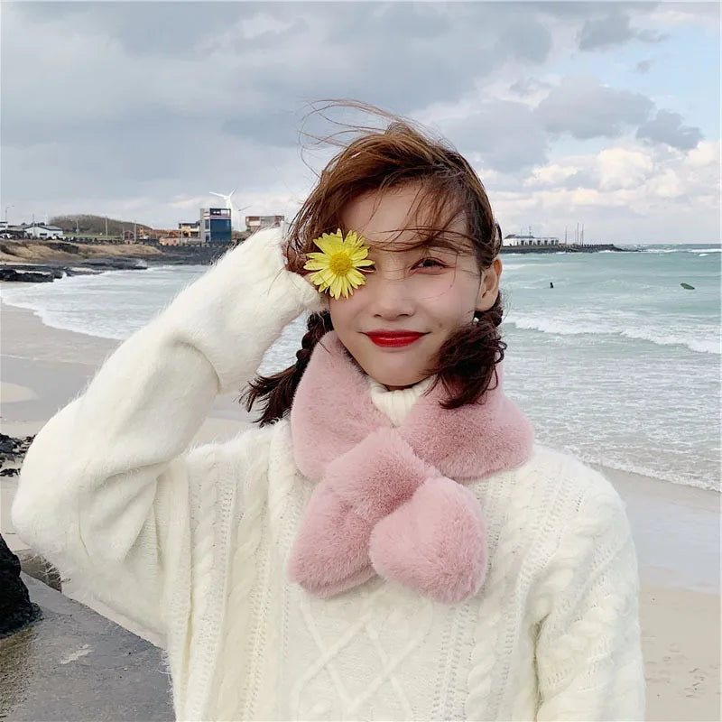 Woman wearing a pink cosy faux fur scarf for cold weather with a flower in her hair by the seaside