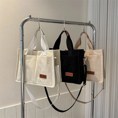 Three large capacity canvas handbags in beige and black displayed on a rack for stylish accessory lovers