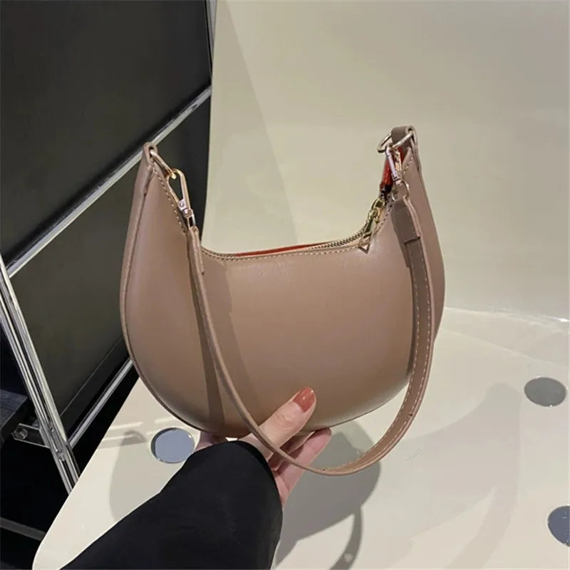 Luxury moon-shaped handbag in beige held by a hand, featuring a sleek design and a stylish strap