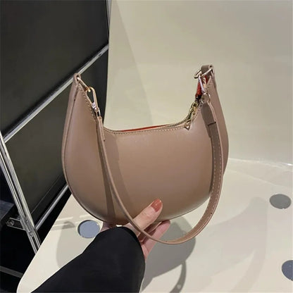 Luxury moon-shaped handbag in beige held by a hand, featuring a sleek design and a stylish strap