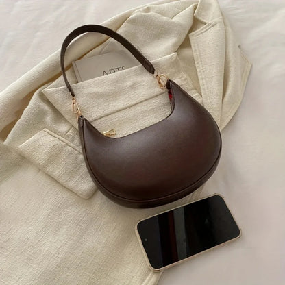 Luxury moon-shaped handbag in brown leather with a stylish handle, placed next to a smartphone
