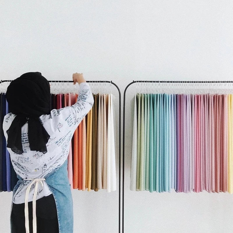 A woman selecting colours from a display of chiffon fabrics, showcasing Muslim chiffon hijab scarf options